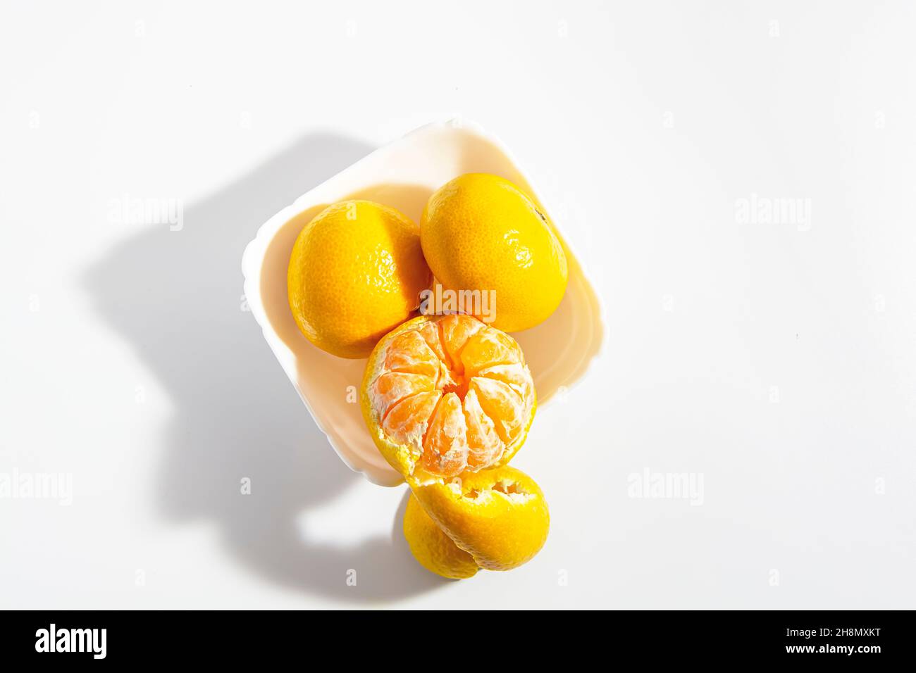 Due tangerini interi e una metà sbucciata in una ciotola bianca quadrata su sfondo bianco. Isolare. Primo piano. Foto orizzontale. Foto di alta qualità Foto Stock
