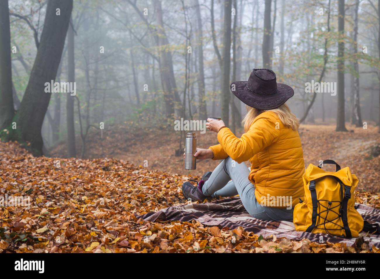 Escursionista seduto su coperta da picnic e bere bevande calde nella foresta autunnale. Donna che riposa in natura durante l'escursione Foto Stock