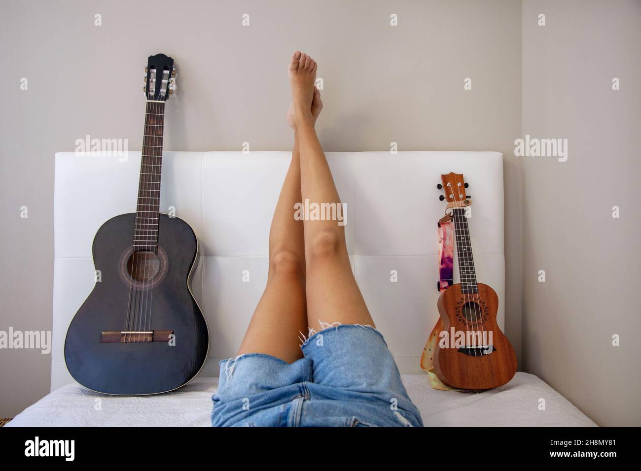 Donna con strumenti a letto. Ragazza con la sua chitarra e il suo ukulele sul letto nella sua stanza a casa. Chitarra spagnola. Foto Stock