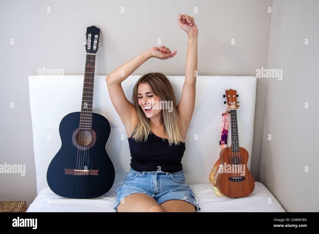 Donna con strumenti a letto. Ragazza con la sua chitarra e il suo ukulele sul letto nella sua stanza a casa. Chitarra spagnola. Foto Stock