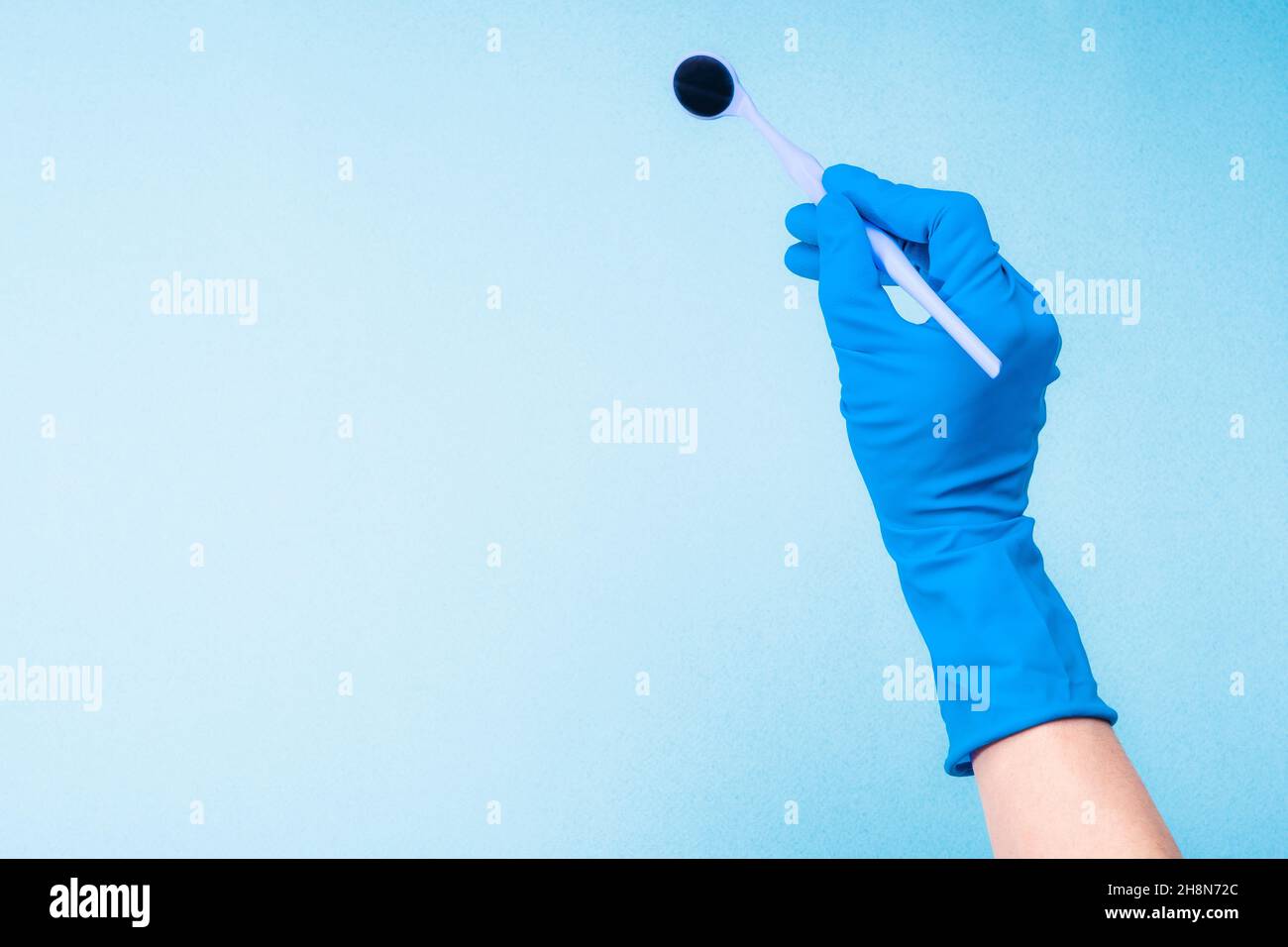Mano nel guanto blu che regge lo specchio dentale Foto Stock