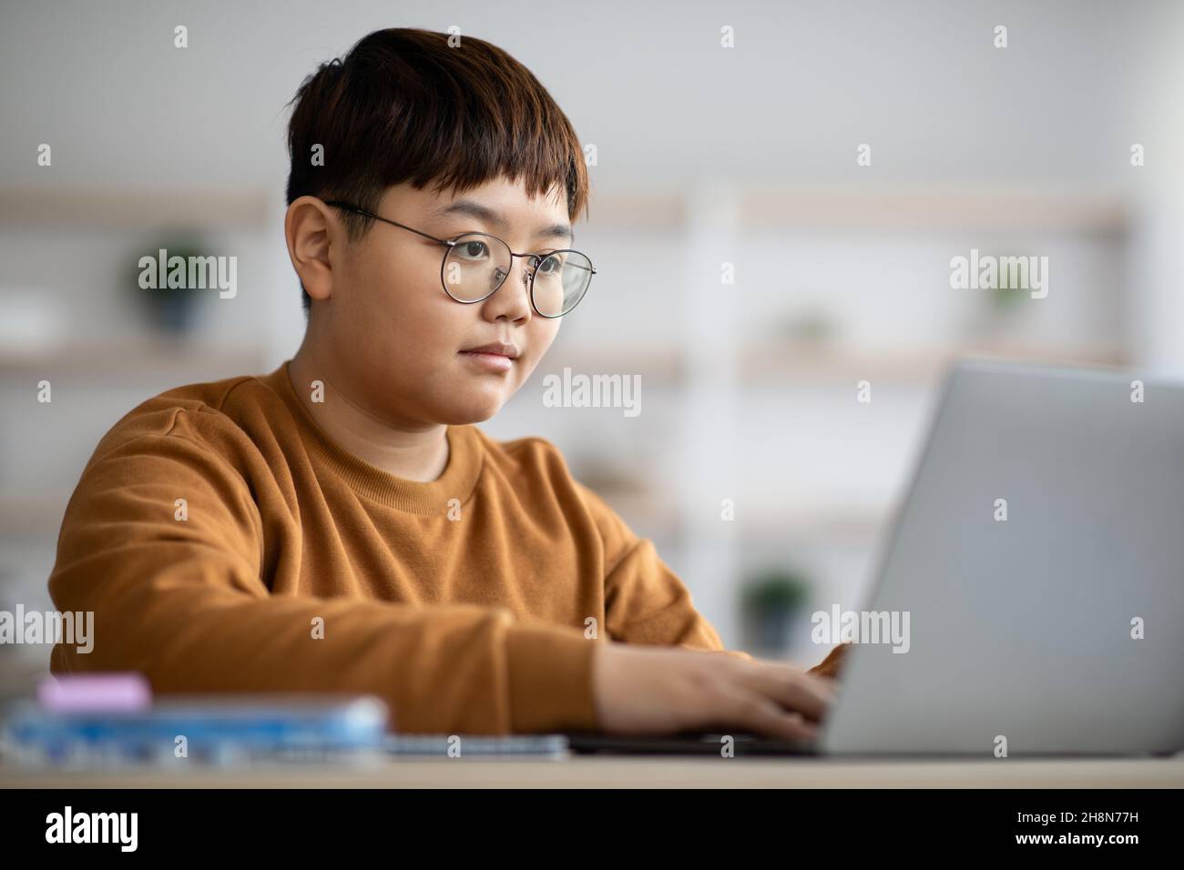 Ragazzo intelligente seduto di fronte al computer portatile, facendo i compiti Foto Stock