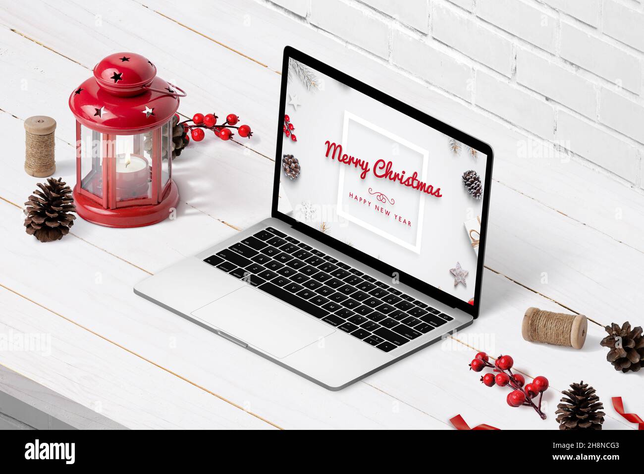 Computer portatile con testo di saluto di buon Natale e felice anno nuovo in mostra. Composizione isometrica su scrivania in legno bianco con decorazioni natalizie Foto Stock