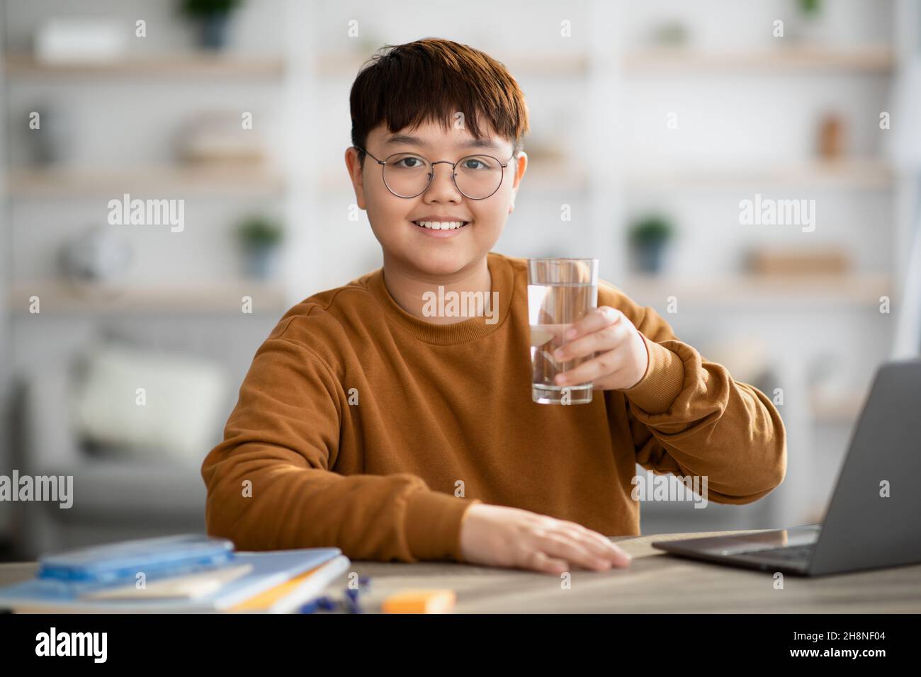 Adolescente asiatico positivo che tiene un bicchiere d'acqua durante lo studio Foto Stock