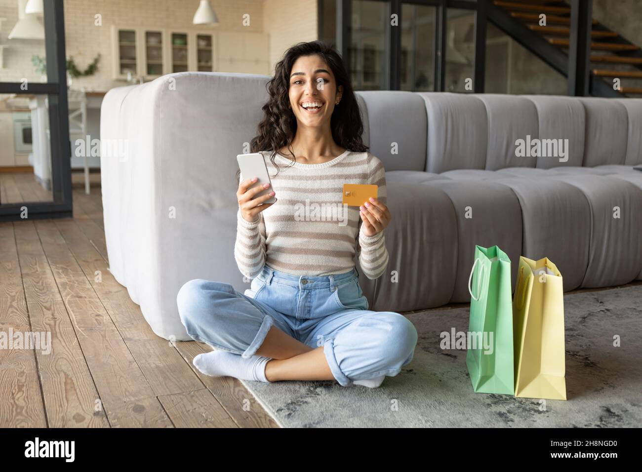 Signora caucasica millenaria che acquista merci via internet, utilizzando smartphone e carta di credito a casa, spazio libero Foto Stock