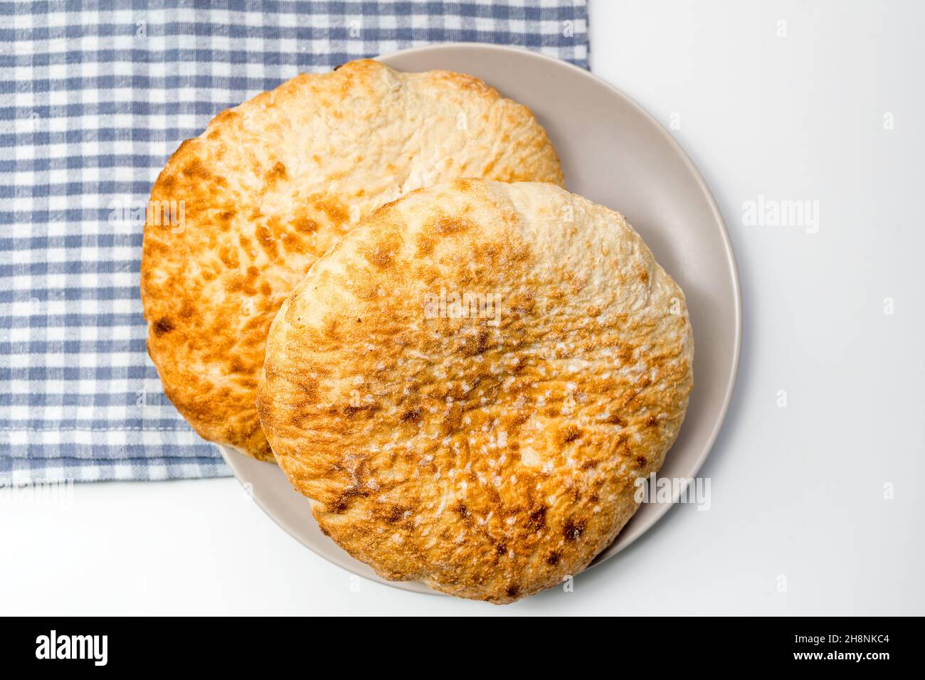 Lafs del pane rotondo piatto del grano in un piatto, su un panno blu della cucina sopra il tavolo bianco Foto Stock