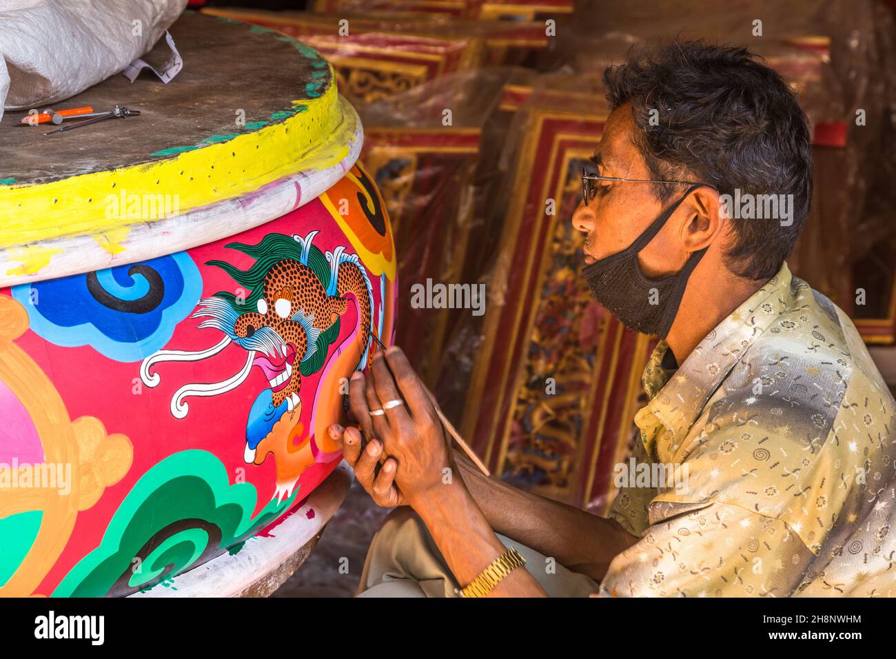 Un uomo nepalese che dipinge un drago su un tamburo rituale tibetano in un laboratorio a Kathmandu, Nepal. Foto Stock