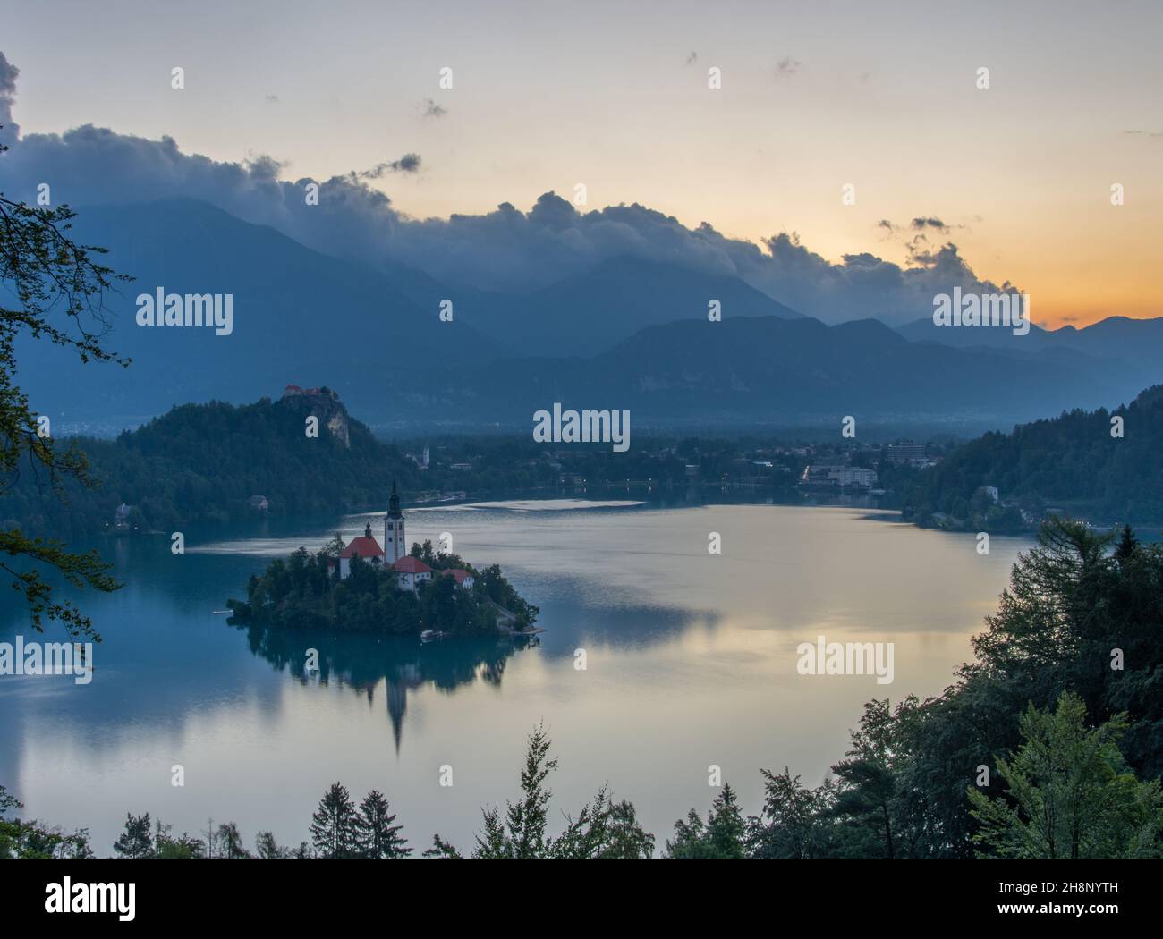 Piccola isola con Chiesa cattolica nel lago di Bled, Slovenia all'alba con il castello e le montagne sullo sfondo. Nell'estate 2020. Foto Stock