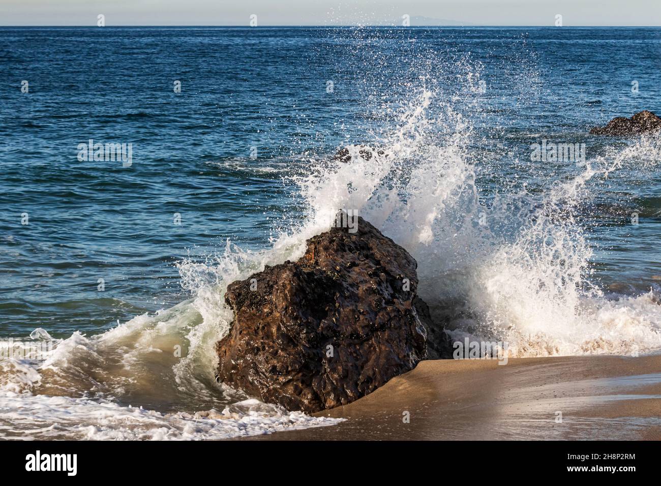 Onde che si schiantano sulla roccia alla spiaggia di Malibu, California. Bagnate la sabbia marrone in primo piano, spruzzate nell'aria. Oceano Pacifico sullo sfondo. Foto Stock