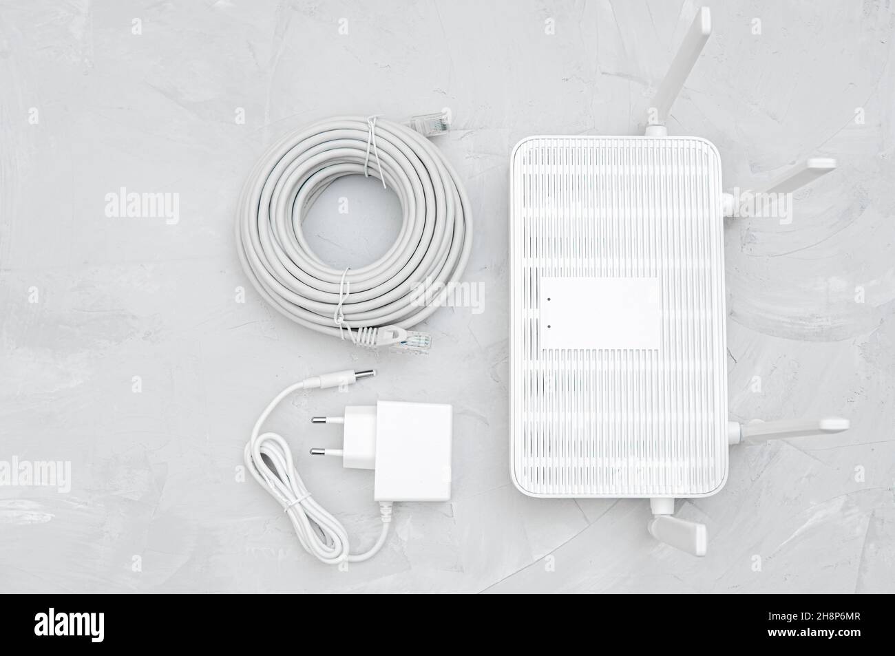 Vista dall'alto di un router Wi-Fi 6 con un adattatore di alimentazione e un rotolo di cavo ethernet su un tavolo in cemento Foto Stock