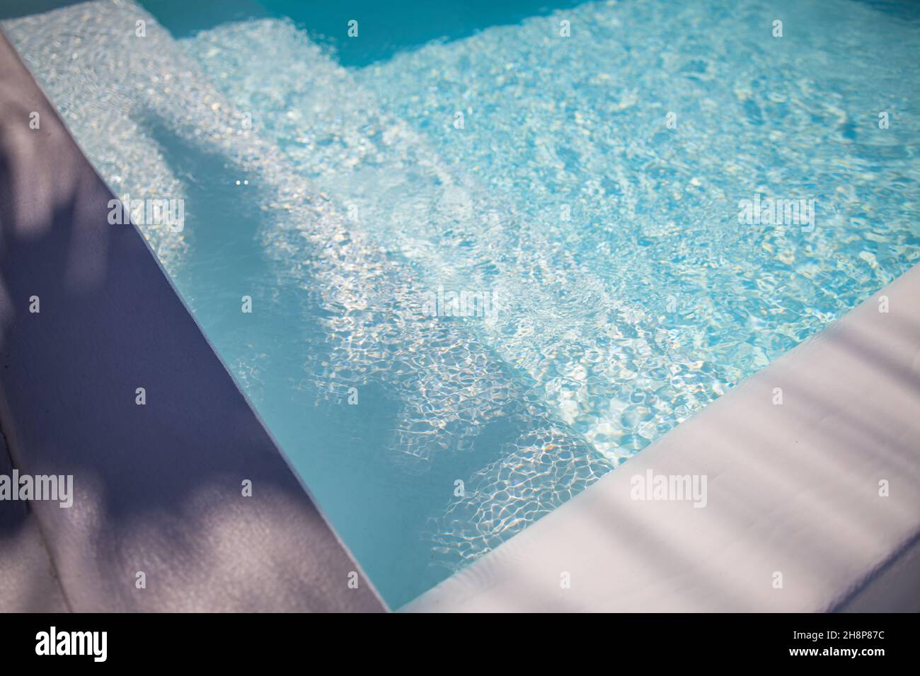 Sfondo astratto della piscina. Relax estivo e concetto ricreativo, acqua blu strappata con scale in piscina, sole onde sfocate. Foto Stock