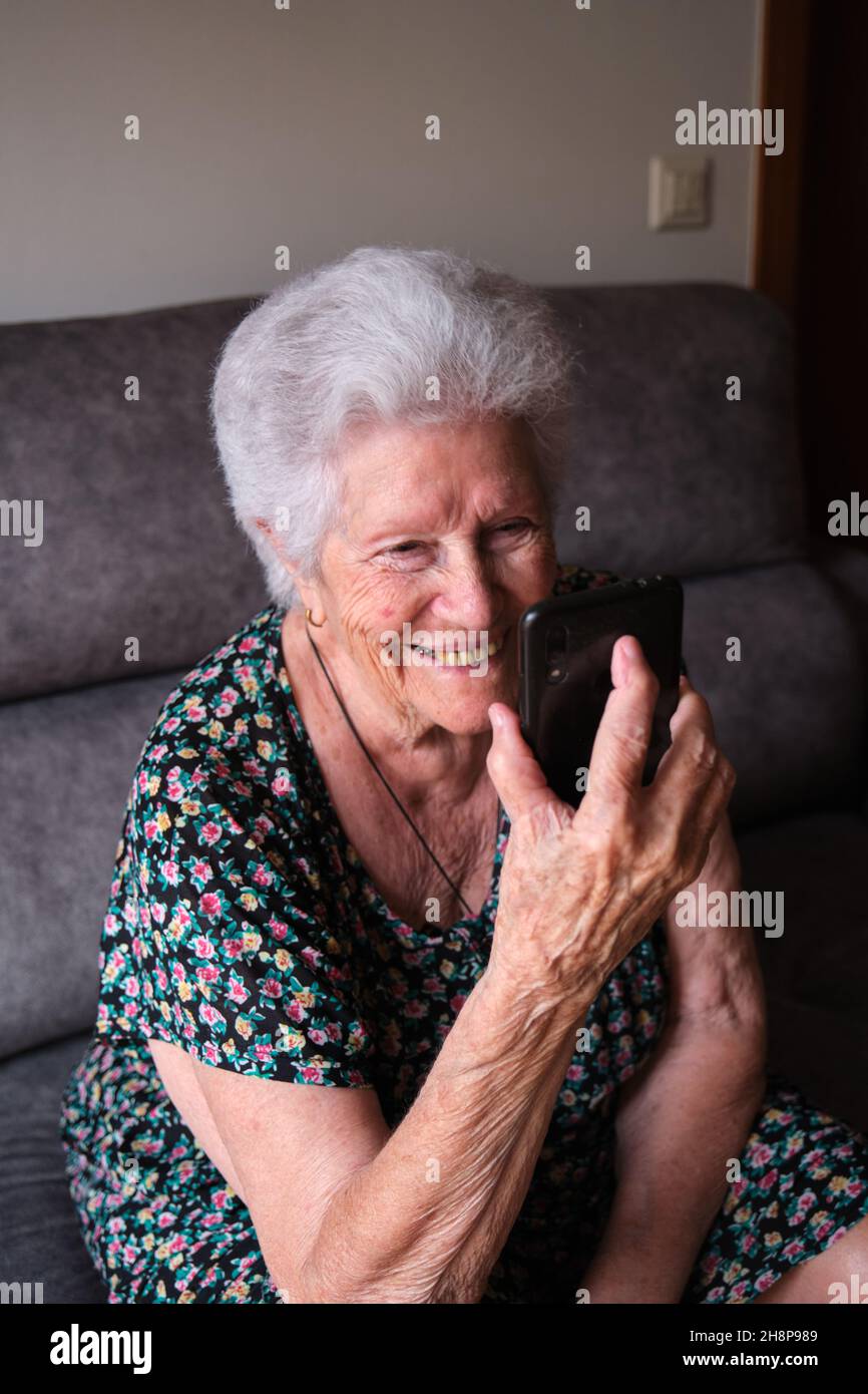 Felice donna anziana che usa uno smartphone per videochiamare parenti o amici. Foto Stock