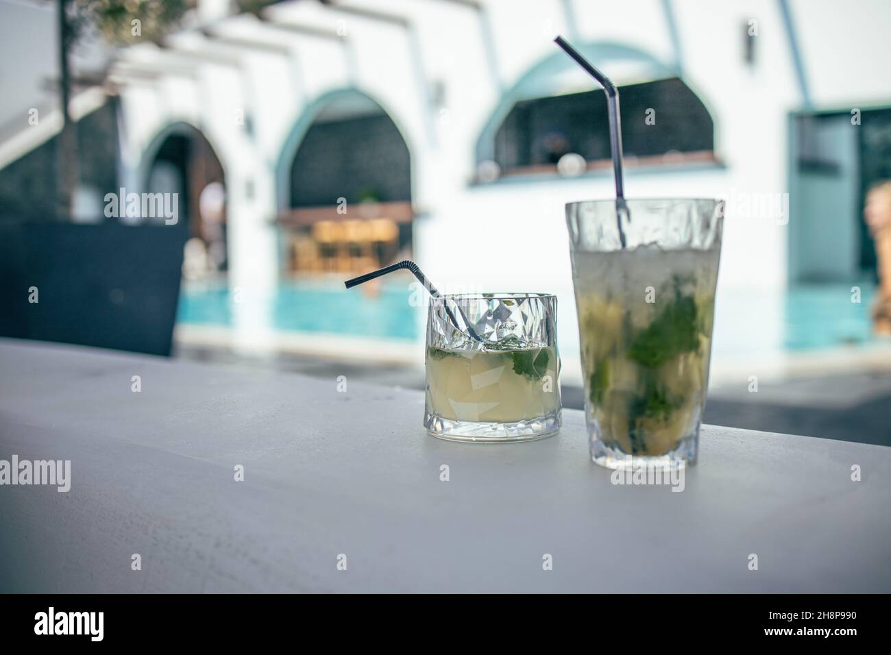Cocktail Mojito ai margini di una piscina del resort. Concetto di vacanza di lusso. Piscina all'aperto sullo sfondo. Bicchieri da cocktail a bordo piscina, piscina sfocata Foto Stock