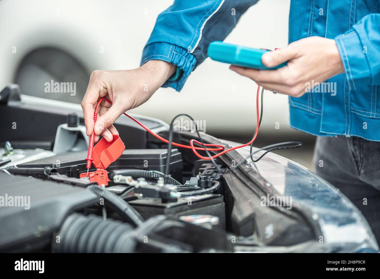 L'elettricista o il meccanico controlla la tensione nella batteria dell'auto all'interno del motore dell'auto con il cofano aperto. Foto Stock