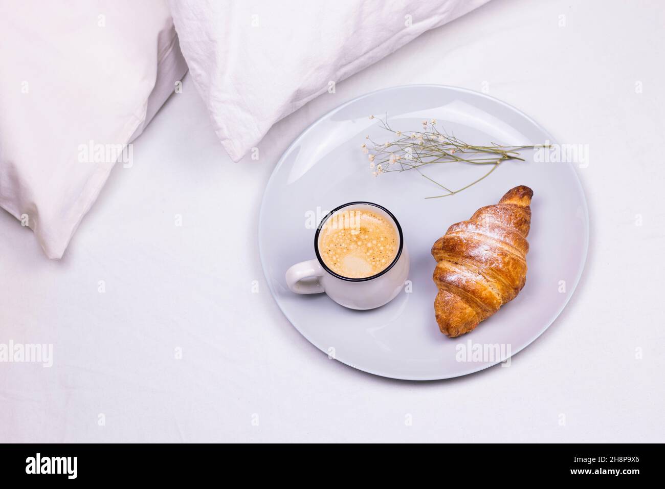 Tazza di caffè con croissant e fiori secchi sul piatto. Colazione al mattino a letto Foto Stock