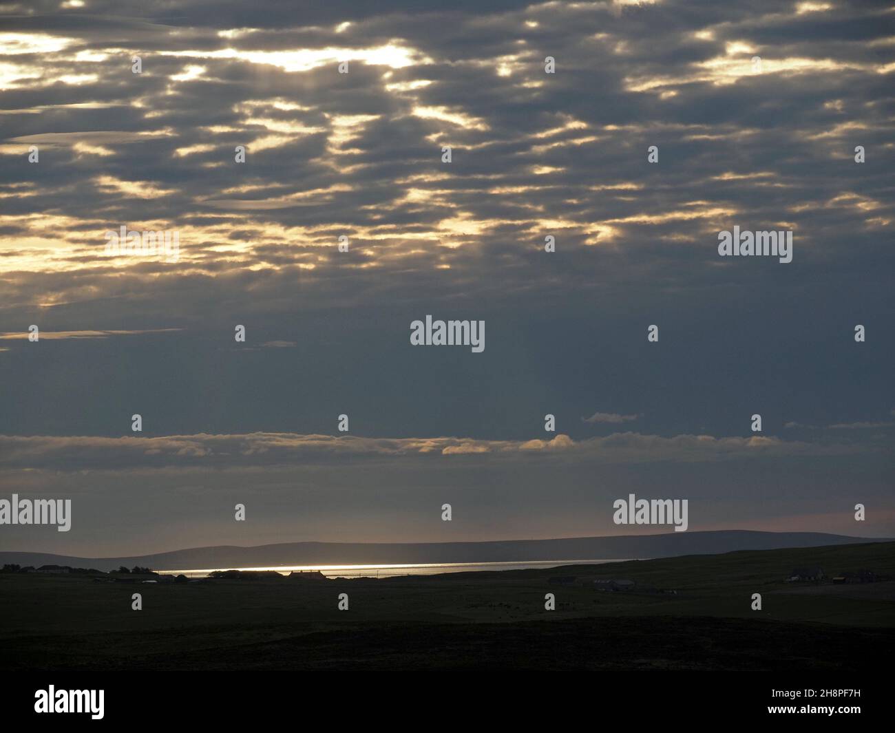luce aurora dorata che brilla sul mare d'argento sotto le nuvole che si ergono nel cielo sgombro all'alba a Orkney, Scozia, Regno Unito Foto Stock