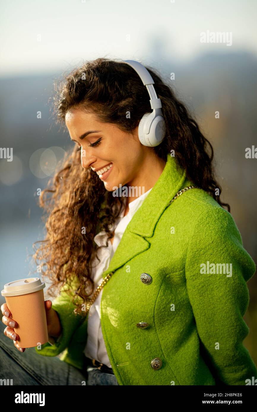 Bella giovane donna che ascolta la musica con smartphone e caffè da asporto sul fiume, nella soleggiata giornata autunnale Foto Stock