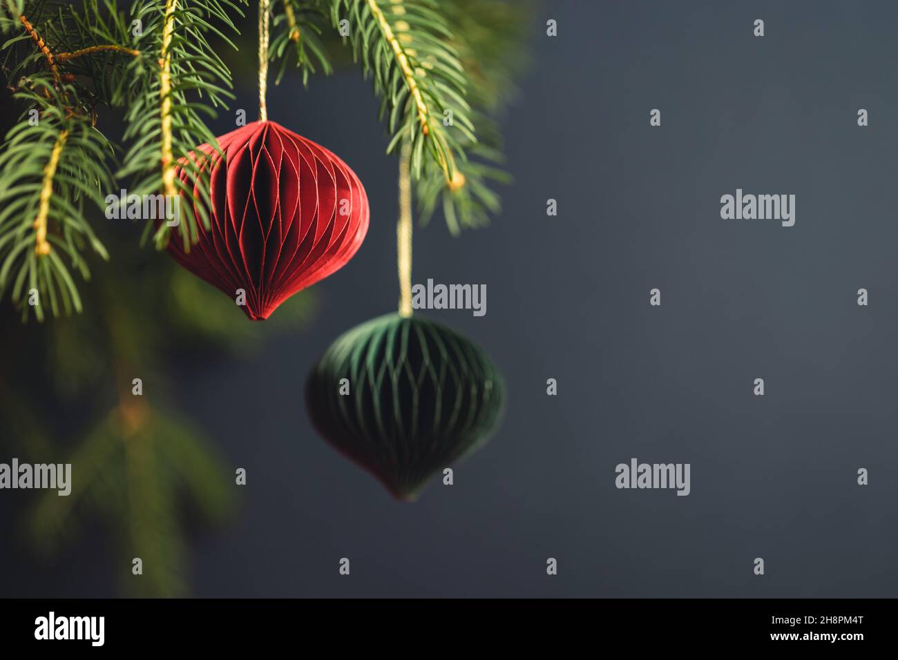 Decorazioni in carta di Natale rossa e verde su rami di abete su sfondo turchese scuro. Foto Stock