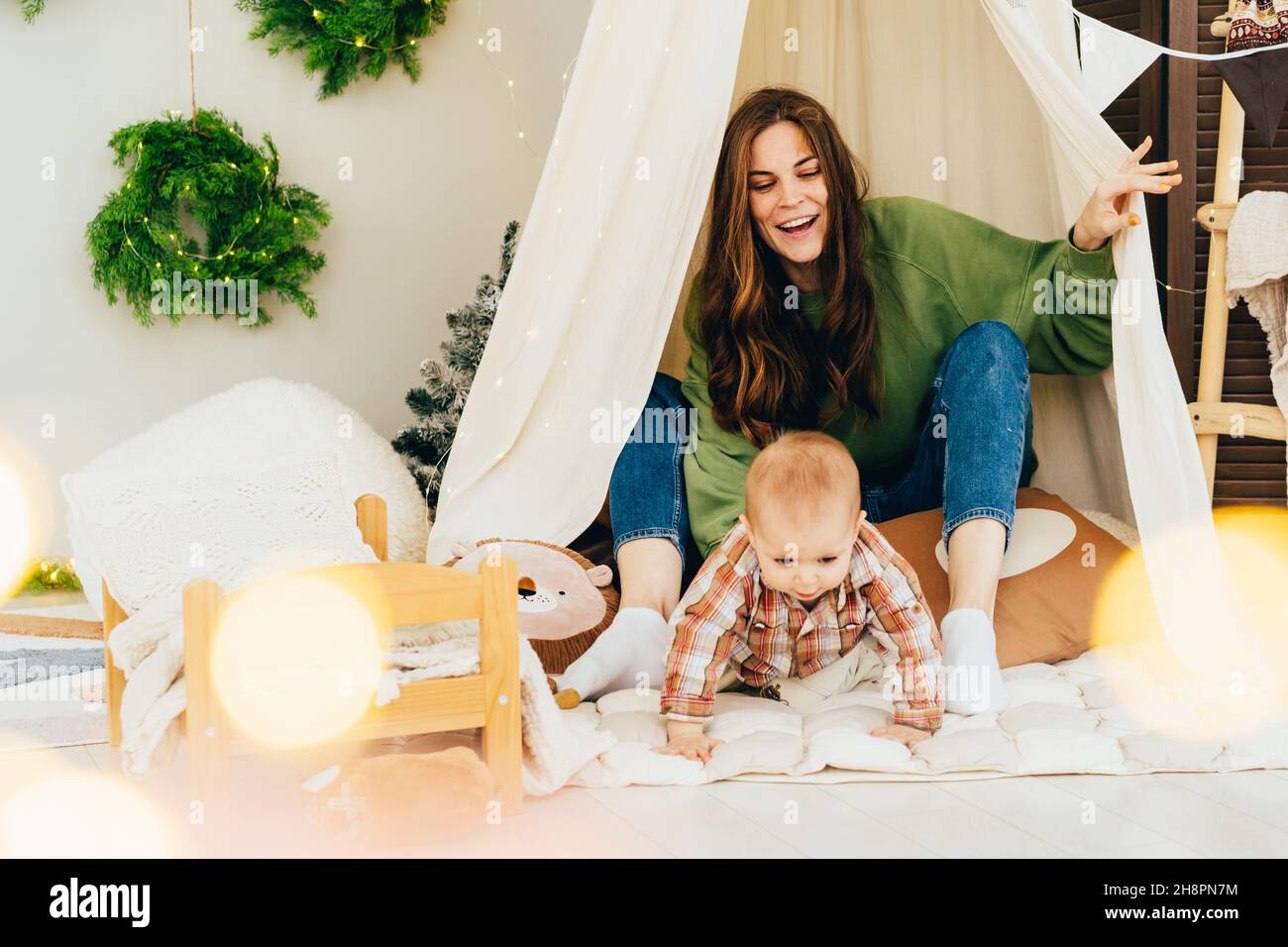 Ride felice giovane rossa mamma giocare con bambino attivo in tenda nella stanza dei bambini. Divertimento per tutta la famiglia, felicità dal passatempo con i bambini. Foto Stock