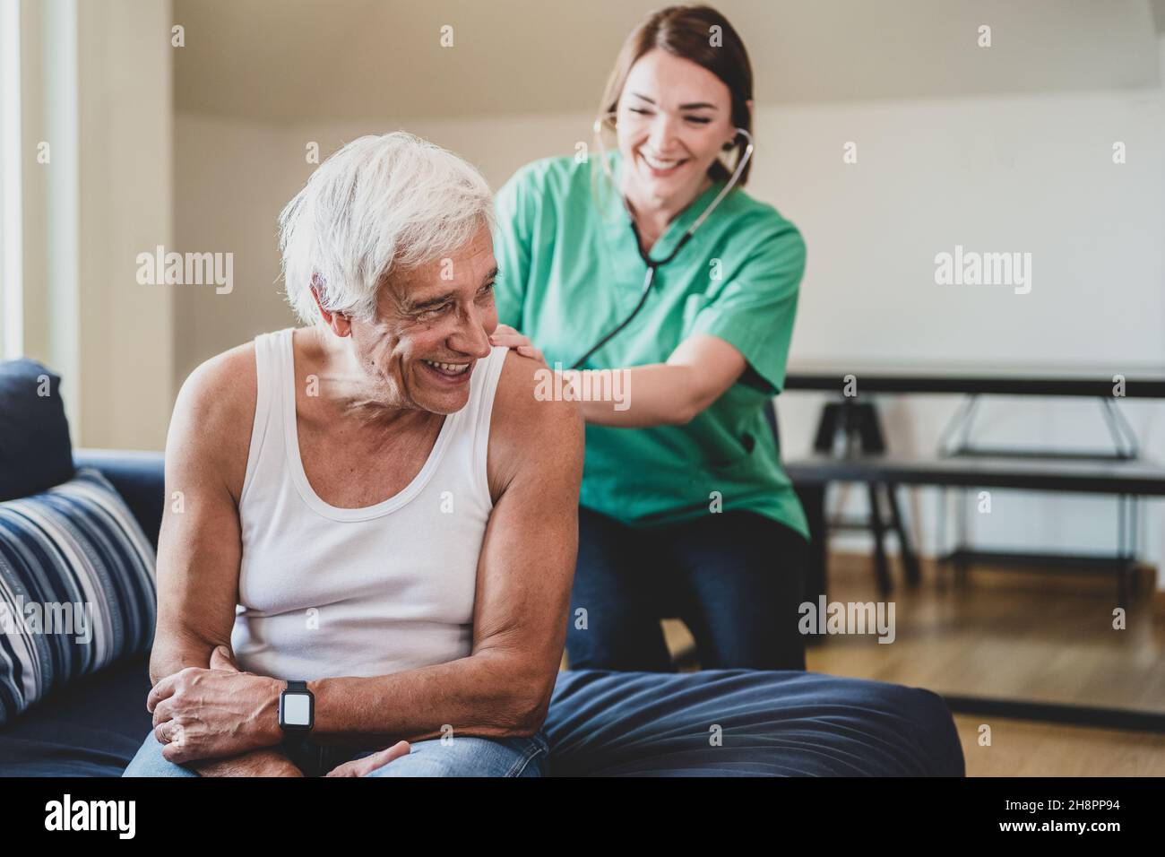 infermiera felice con uno stetoscopio che visita un uomo anziano, assistente medico domestico concetto, sorridente visitatore di salute e un paziente anziano maschio, c Foto Stock