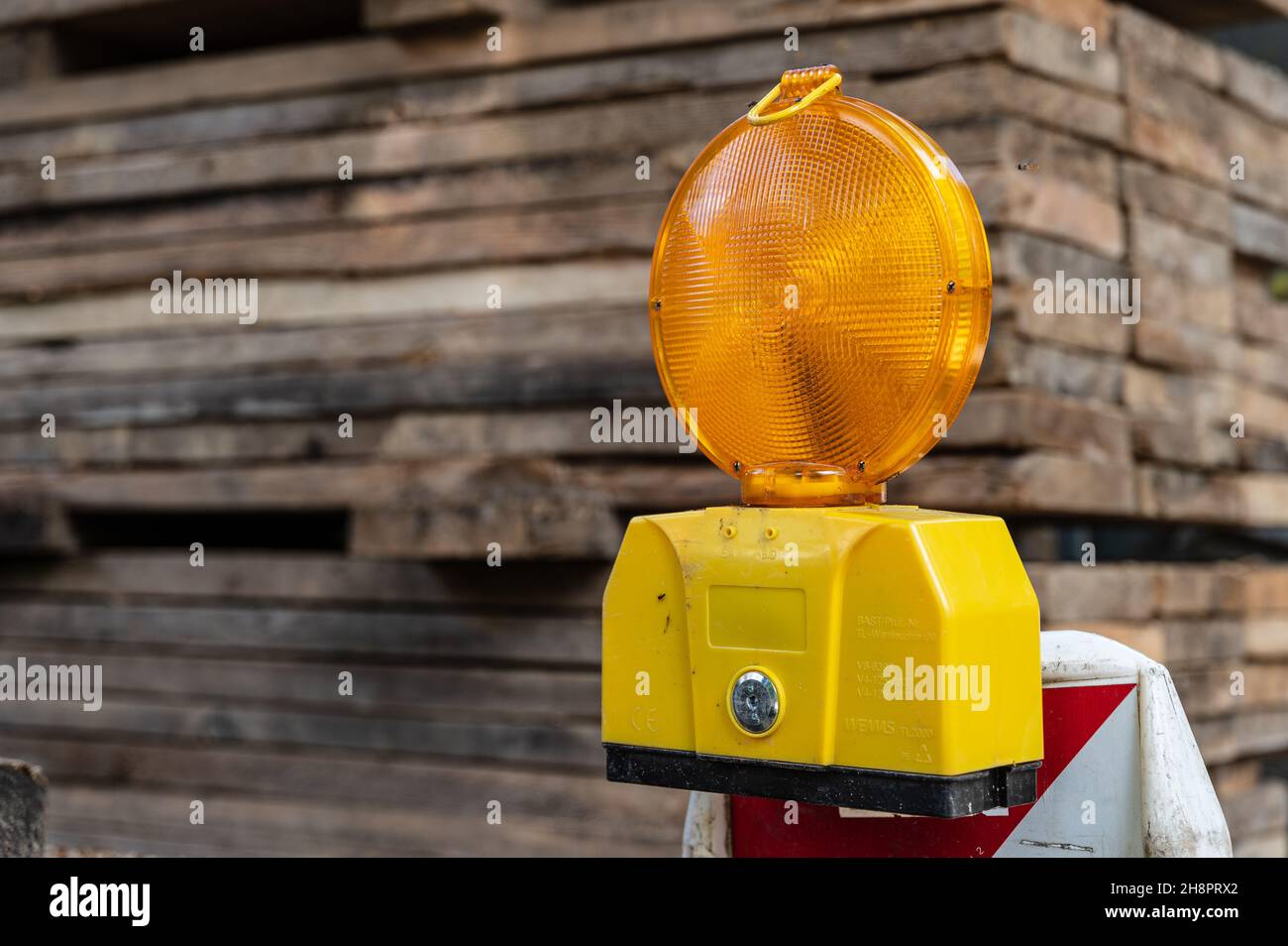 Lampeggiatore di avvertimento arancione da Wemas su una barriera di cantiere con un mucchio di tavole sullo sfondo Foto Stock