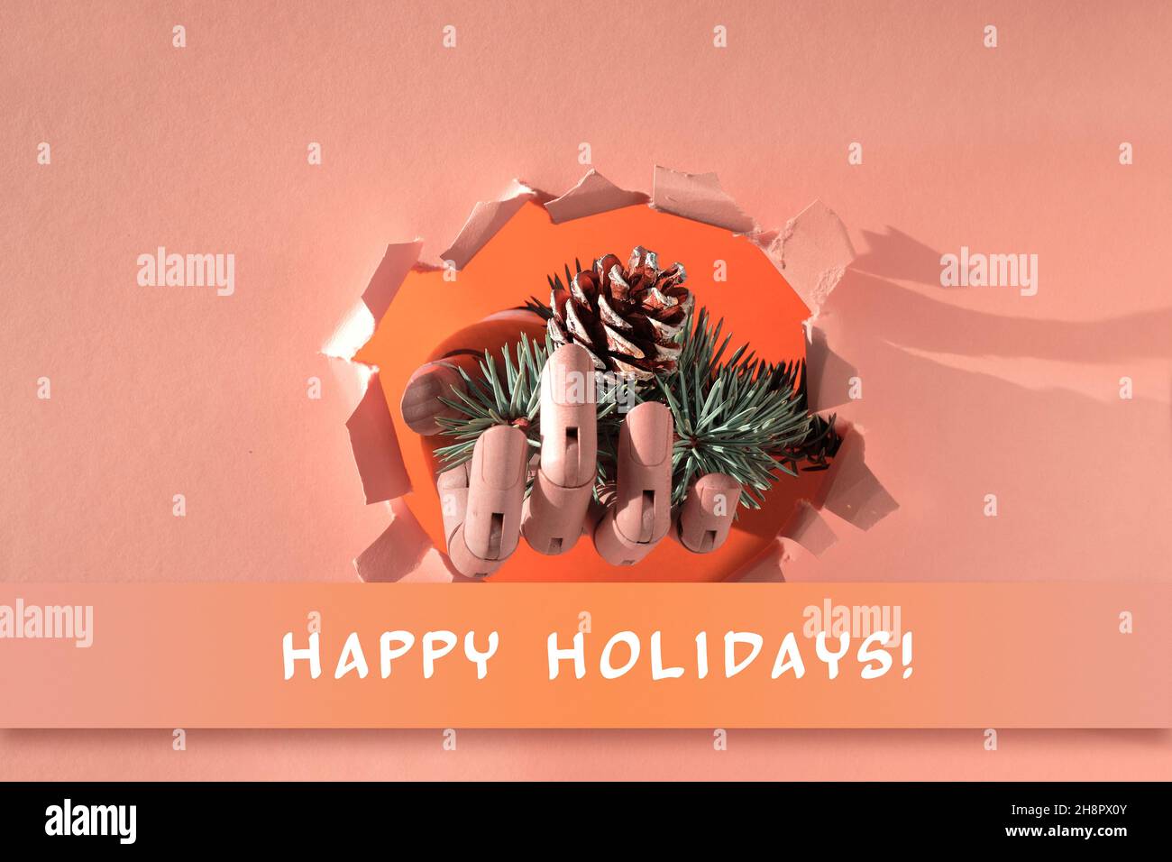 Buon Natale, mano con i rametti di abete e cono attraverso il foro di carta. Fondo creativo minimal concept con lunga ombra su carta beige e arancione. Foto Stock