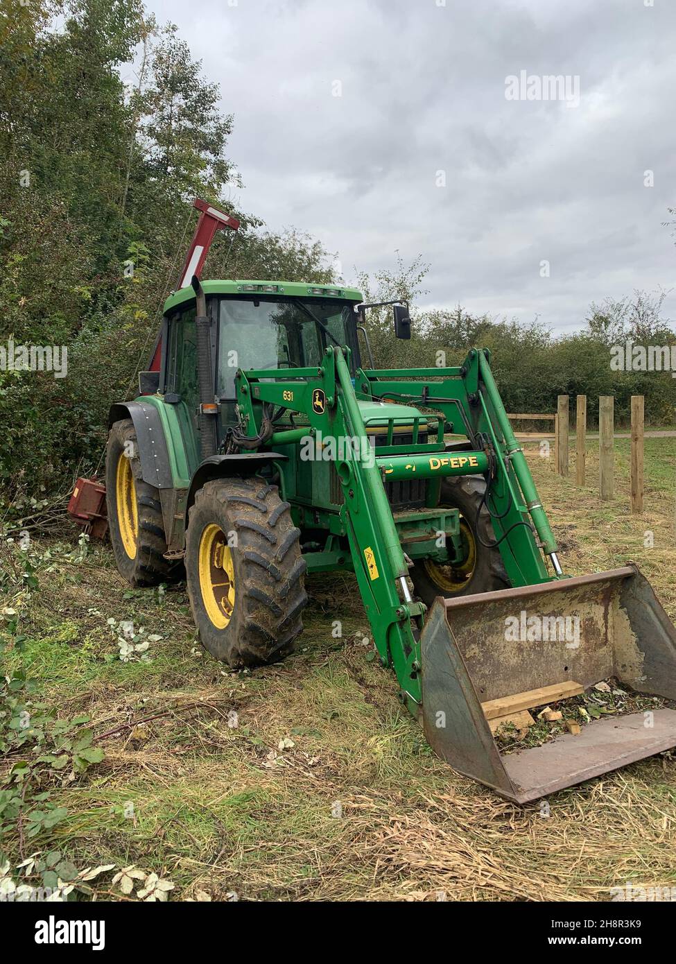 Green digger in campo Northamptonshire UK attrezzatura agricola attrezzatura verde secchio attrezzatura campo campi di raccolta di colore brillante hedgerow pali di legno Foto Stock