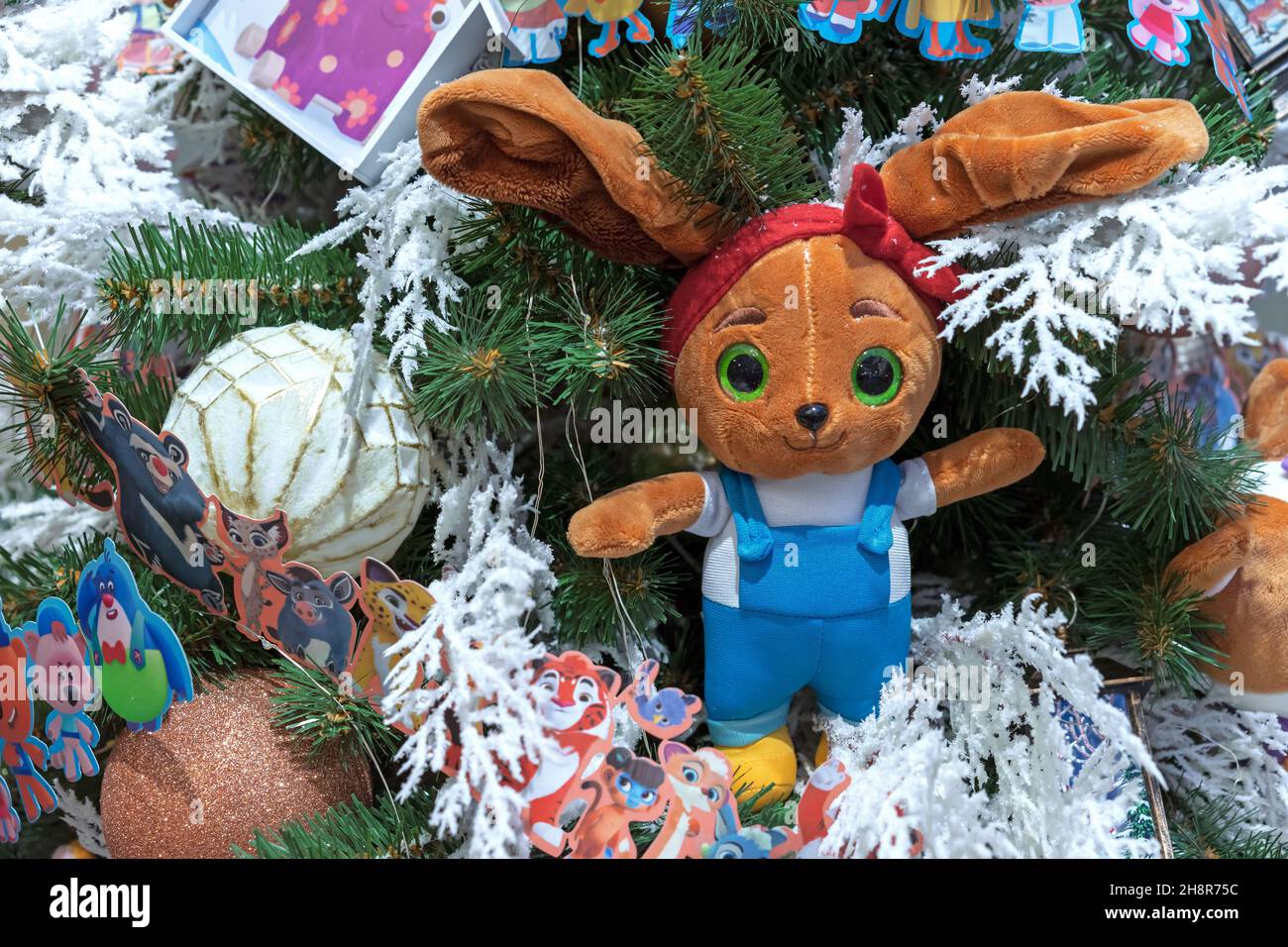 Coniglietto peluche con grandi orecchie su un albero di Natale decorato e coperto di neve. Foto Stock