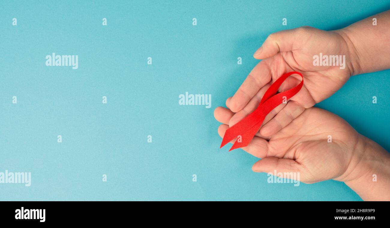 Mani con nastro rosso per la consapevolezza dell'AIDS, sfondo blu con spazio di copia per il testo Foto Stock