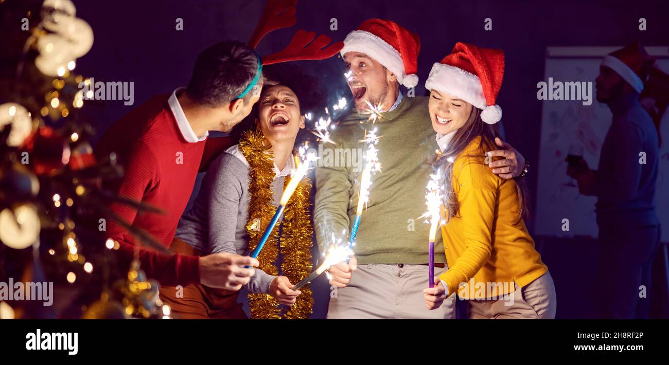 Amore e festa la vigilia di Capodanno. Un piccolo gruppo di amici multiculturali in piedi al buio a mezzanotte con fuochi d'artificio a mano nelle loro mani e hu Foto Stock