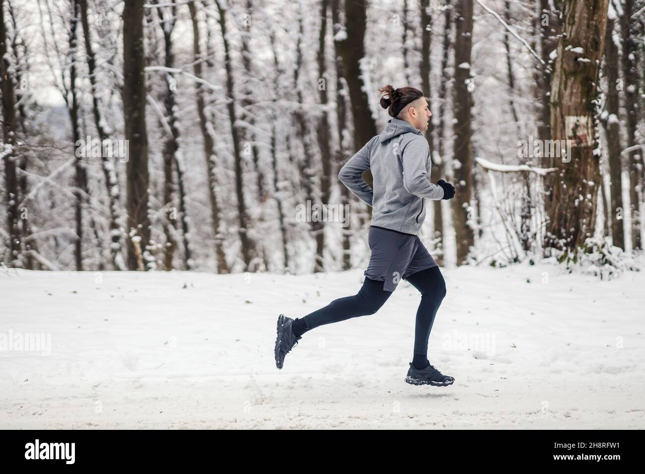 Sportivo che corre nei boschi durante la nevosa giornata invernale. Esercizi cardiovascolari, fitness invernale, fitness all'aperto Foto Stock