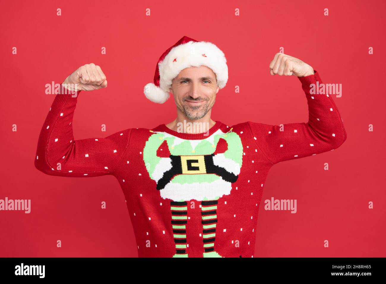 Il potere del Natale. L'elfo di Natale mostra la sua forza. Babbo Natale uomo sorriso braccia flessibili. Felice anno nuovo Foto Stock