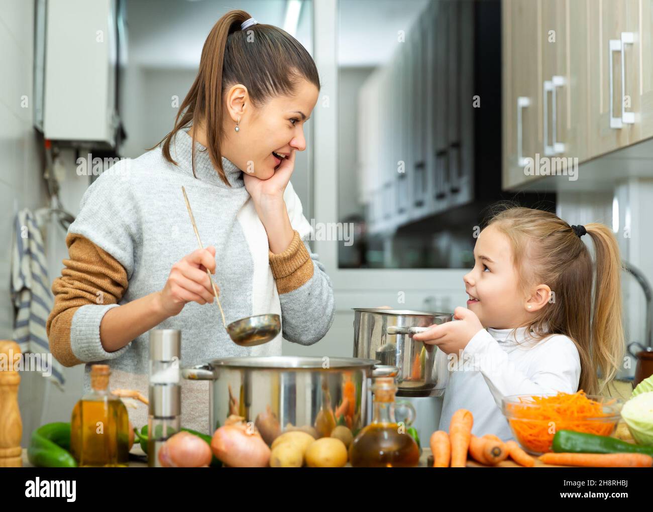 Felice madre giovane e figlia degustazione zuppa di verdure Foto Stock