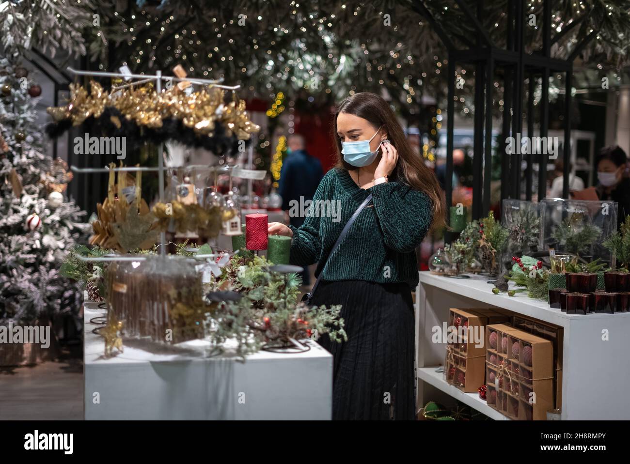Donna in maschera toccare il collo e scegliere le decorazioni mentre si acquista nel centro commerciale moderno prima di Natale Foto Stock