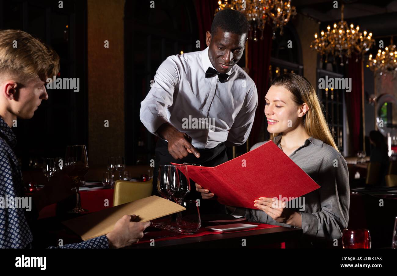 Coppia con menu è dando fine di afro-american cameriere nel ristorante alla moda Foto Stock