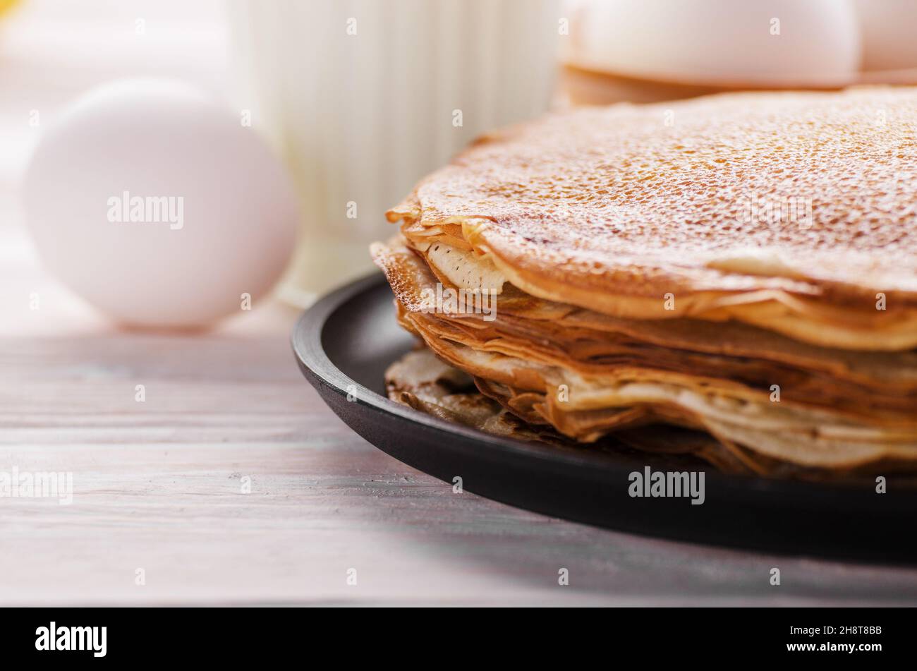 Pila di crepes francese in padella su legno tavolo da cucina con latte uova e farina a parte Foto Stock