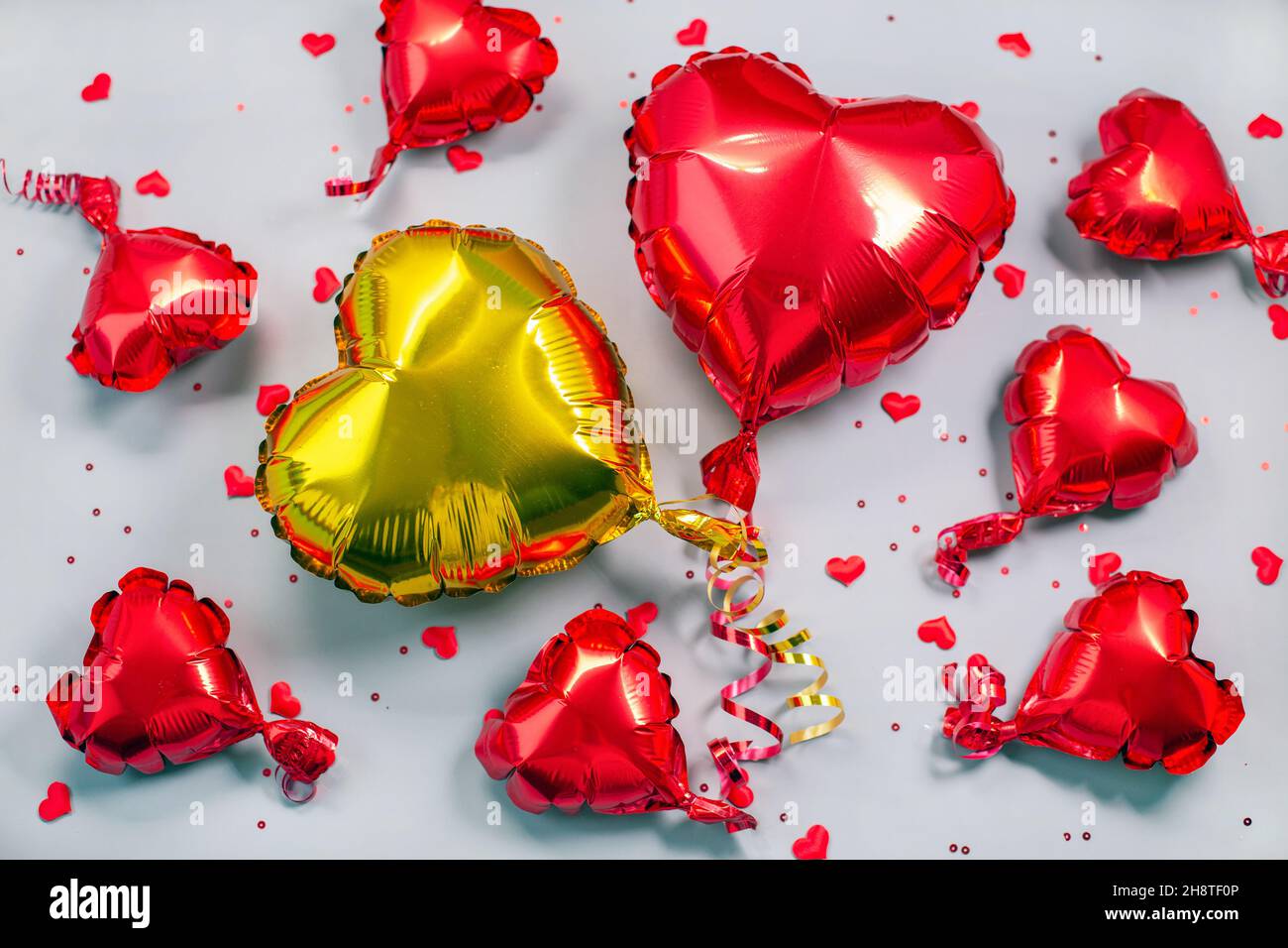 Palloni d'aria rossi e dorati di lamina a forma di cuore su sfondo grigio. Palloncino metallico. Concetto di amore. Festa. San Valentino decorazione o festa. Foto Stock