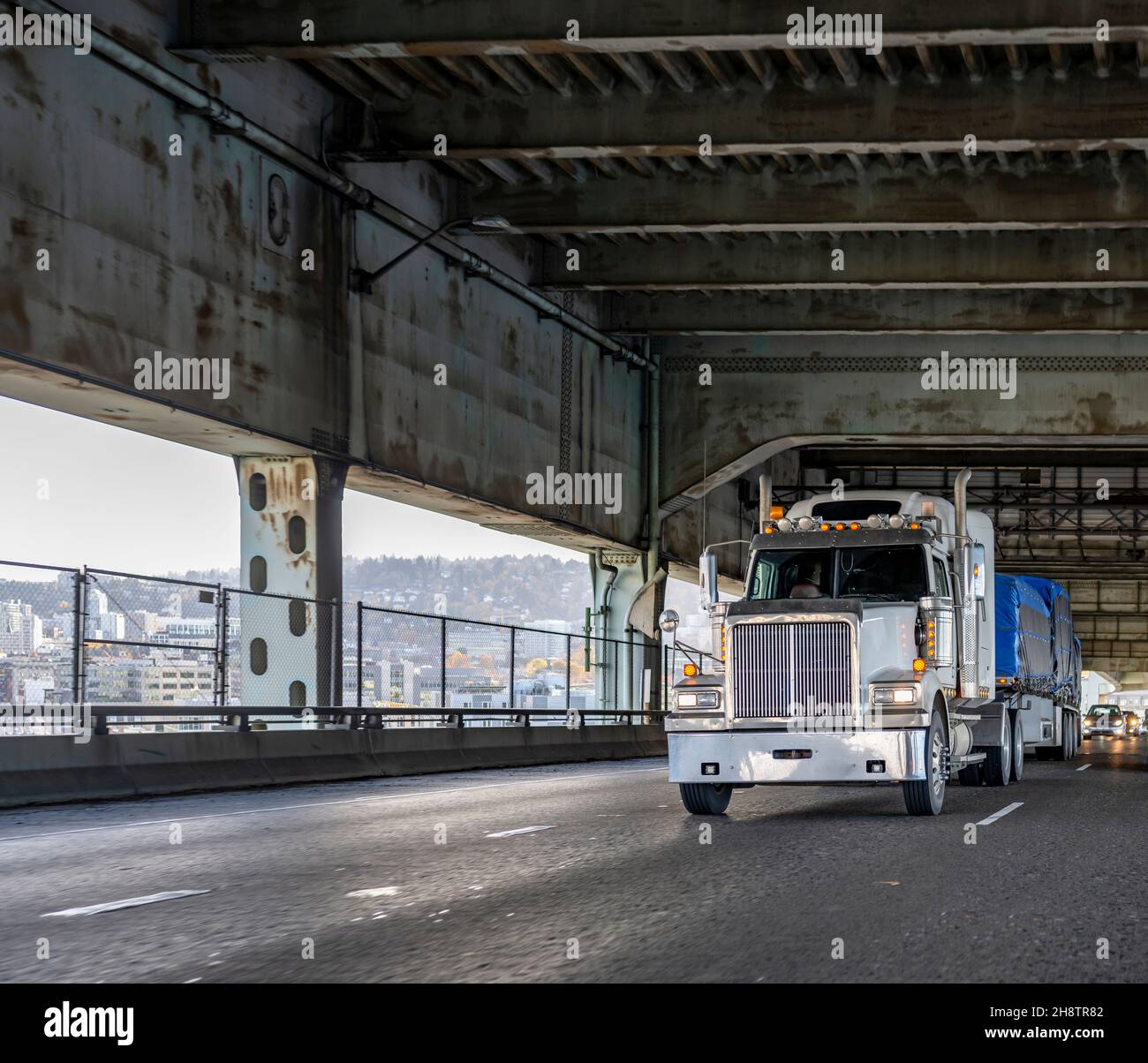 Potente semirimorchio industriale bianco con cofano da banco grande e luci aggiuntive per il trasporto di carichi coperti su un semirimorchio a pianale che gira su Foto Stock