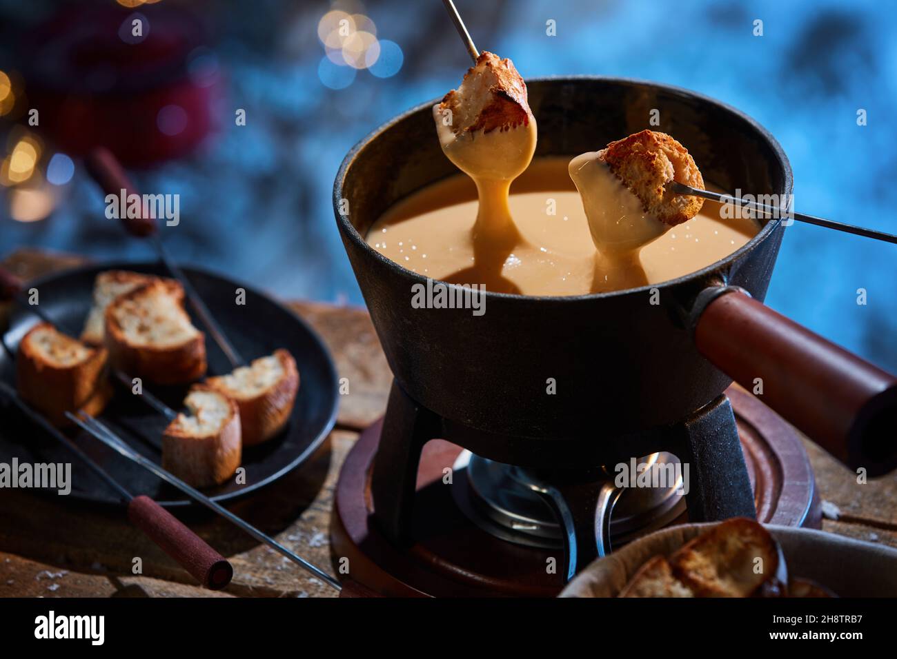 Da sopra di deliziosi crunchy crostini di pane che sono immersi in fonduta di formaggio caldo in pentola posta su tavola di legno in inverno Foto Stock