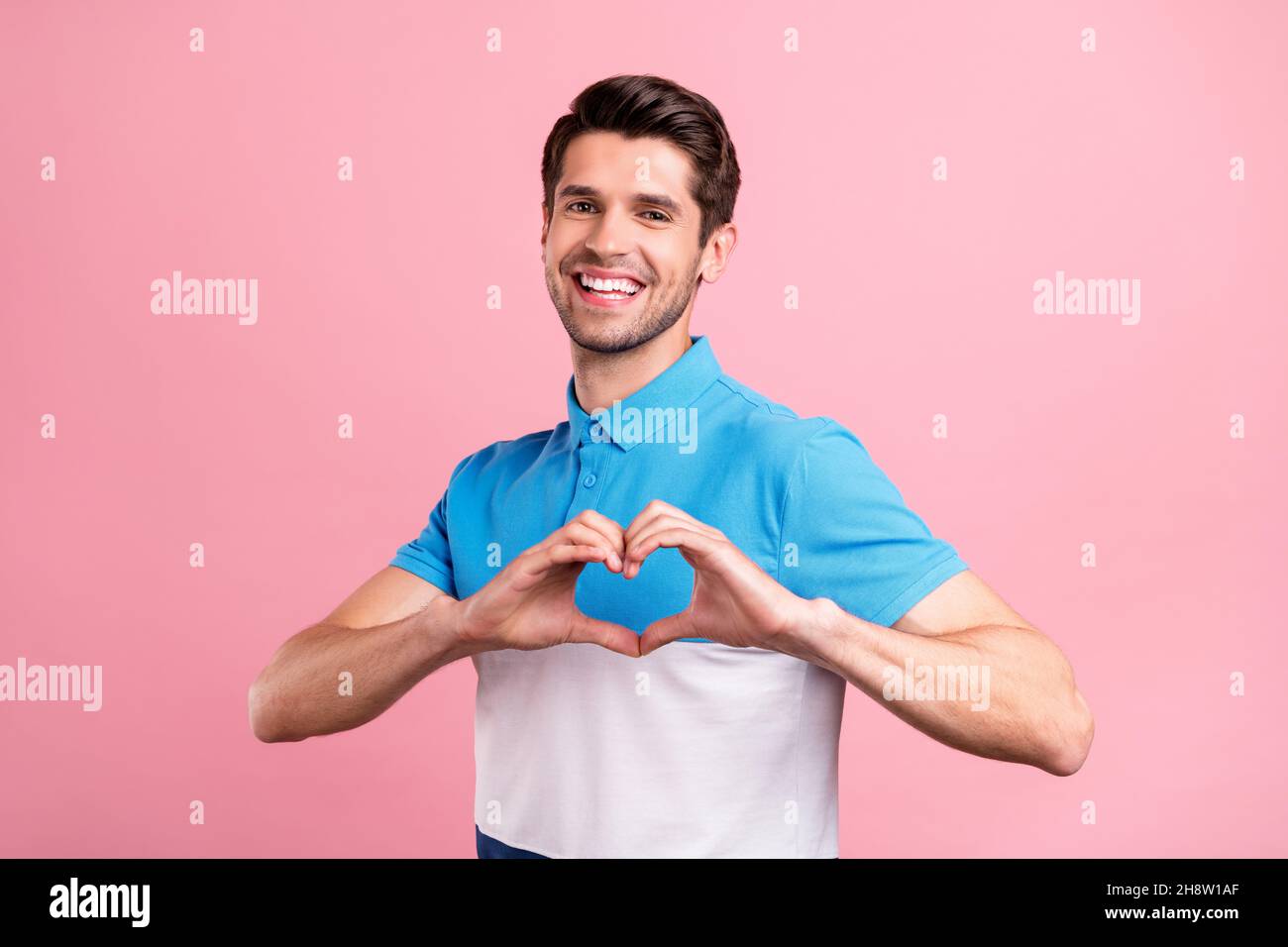 Foto di brunet carino giovane ragazzo show cuore indossare polo a righe isolato su sfondo rosa Foto Stock