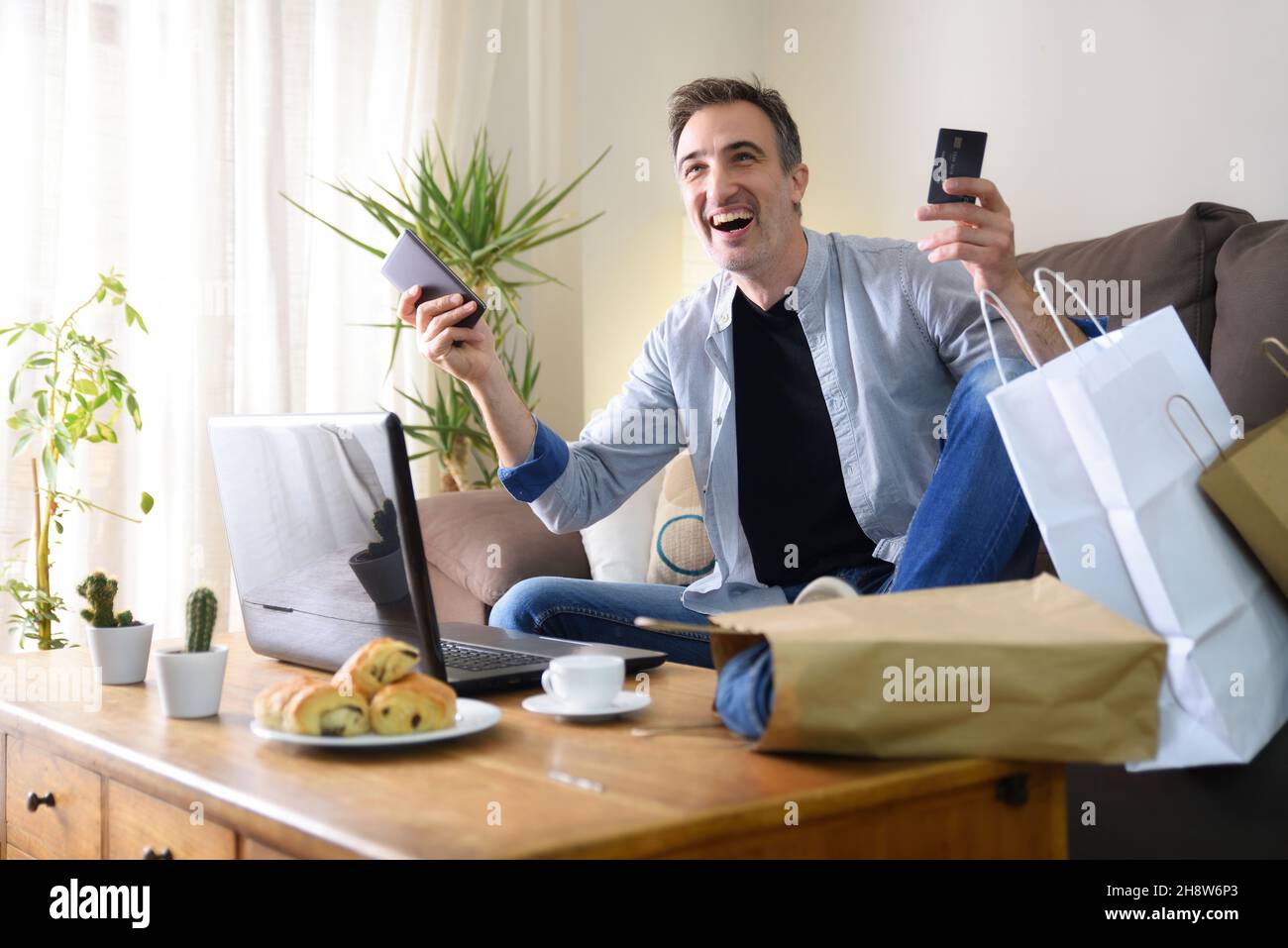 Uomo felice che acquista online da dispositivi elettronici dal divano a casa. Composizione orizzontale. Foto Stock