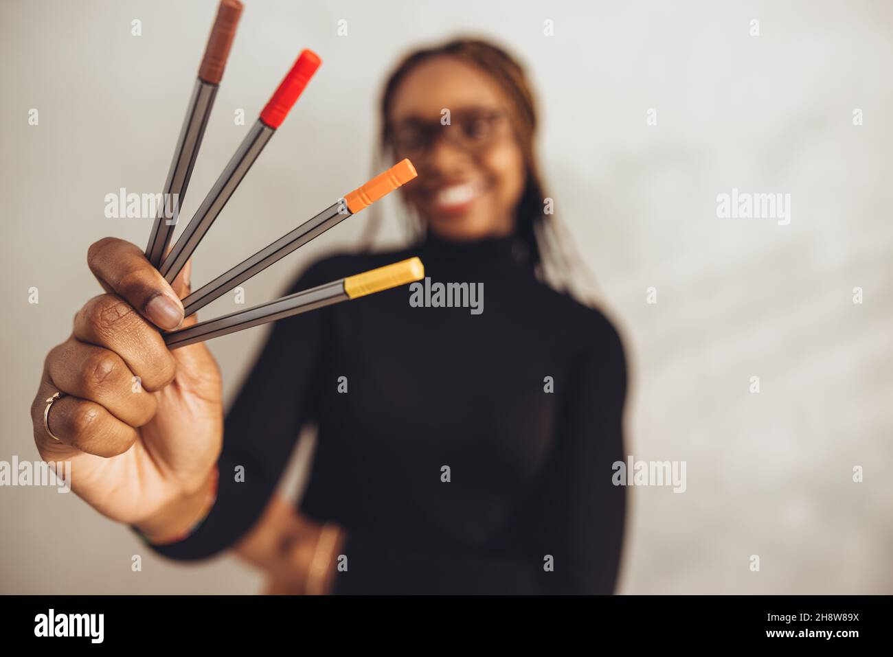Designer creativo che tiene le penne colorate sorridendo allegro sullo sfondo. Felice giovane freelancer in piedi da solo nella sua casa offie. Artistico Foto Stock