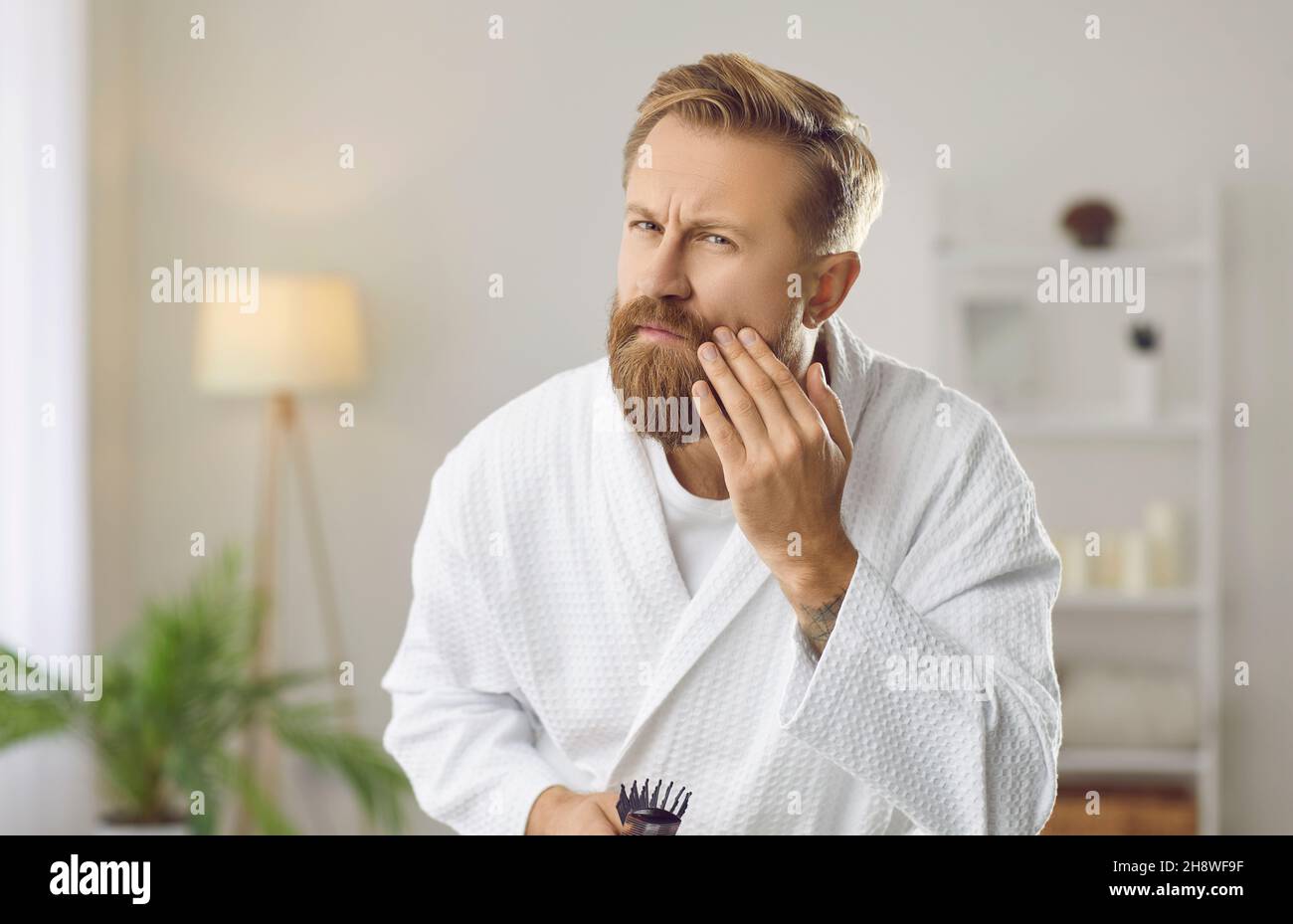 Uomo bello preoccupato che guarda le rughe sul suo viso durante la routine di cura della pelle mattina Foto Stock