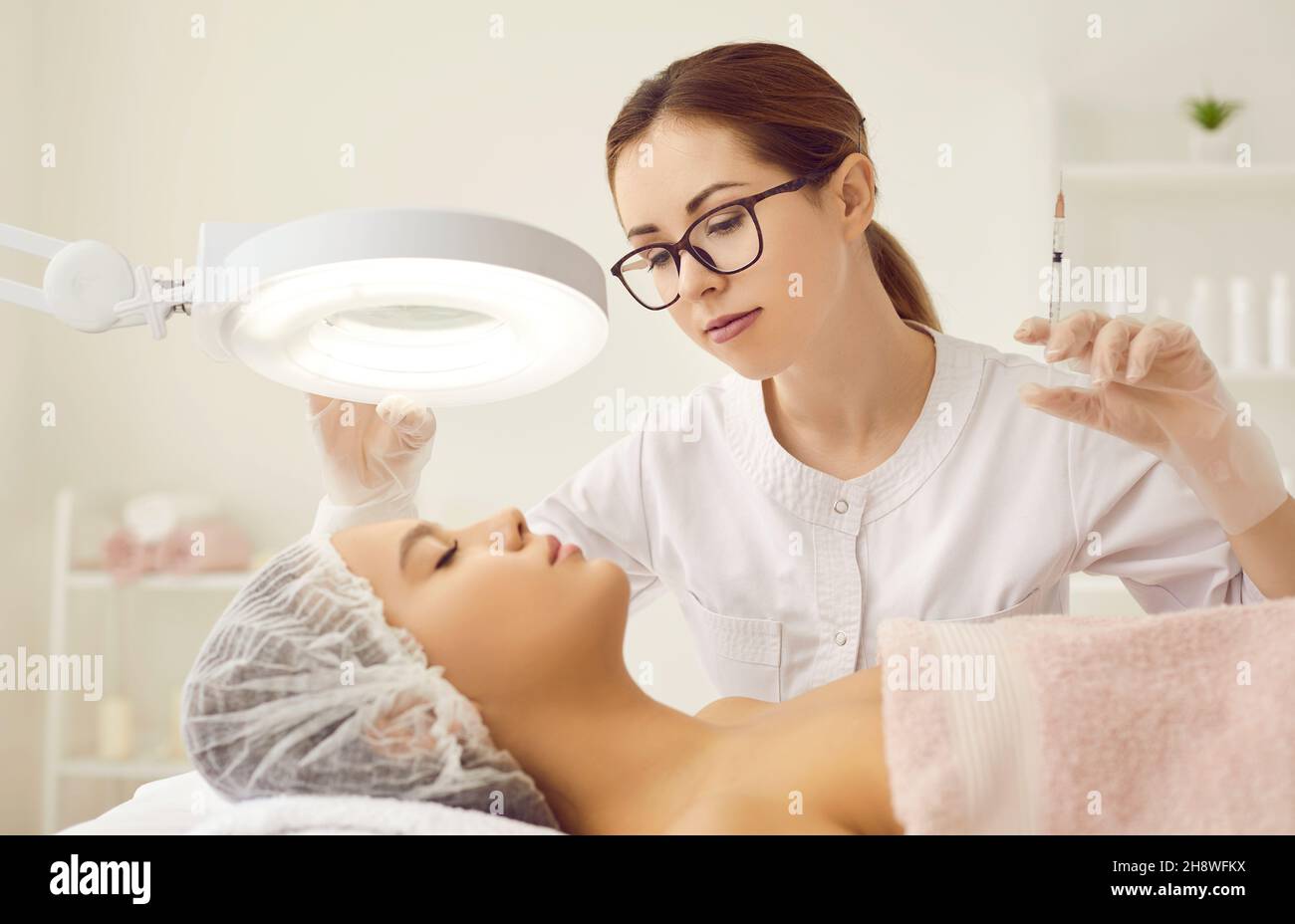 Infermiera in clinica di medicina estetica che dà l'iniezione di bellezza alla donna sotto lampada di ingrandimento Foto Stock