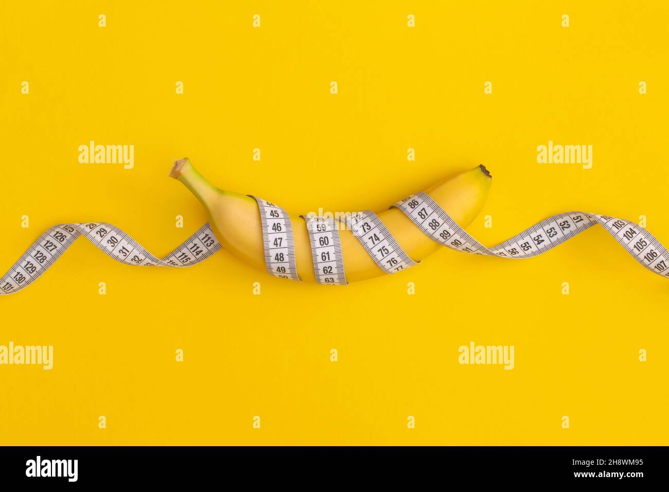 Nastro di misurazione e banana su sfondo giallo. Concetto di perdita di peso Foto Stock