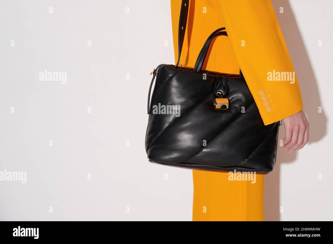 Donna in abito arancione con borsa in pelle nera in mano su sfondo bianco. Borsa tote trapuntata elegante accessorio. Nuova collezione o vendita. Foto Stock