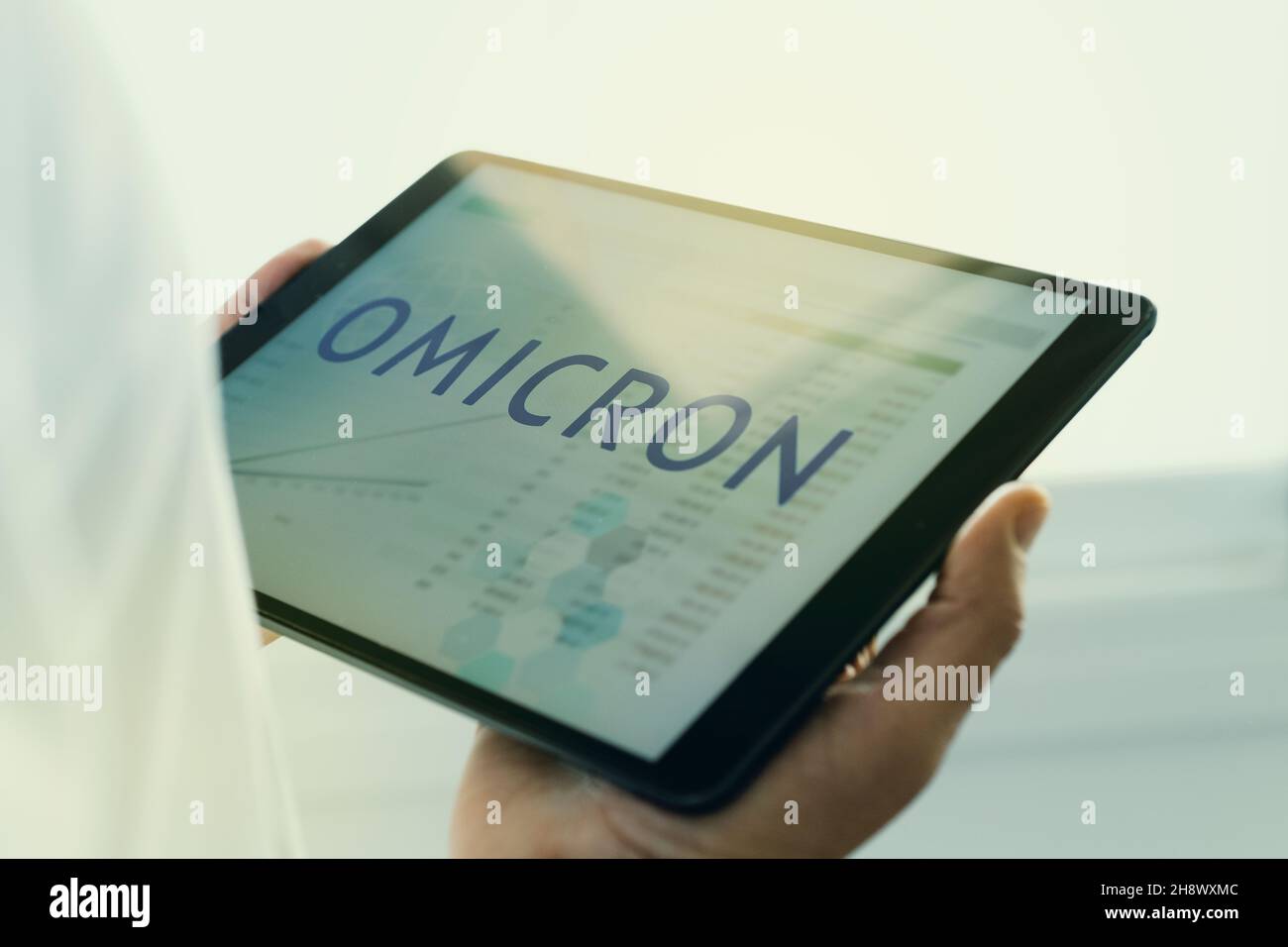 Primo piano di un medico, indossando un cappotto bianco, avendo un tablet digitale in mano con il testo omicron nel suo schermo, per la SARS-cov-2 Omicron va Foto Stock