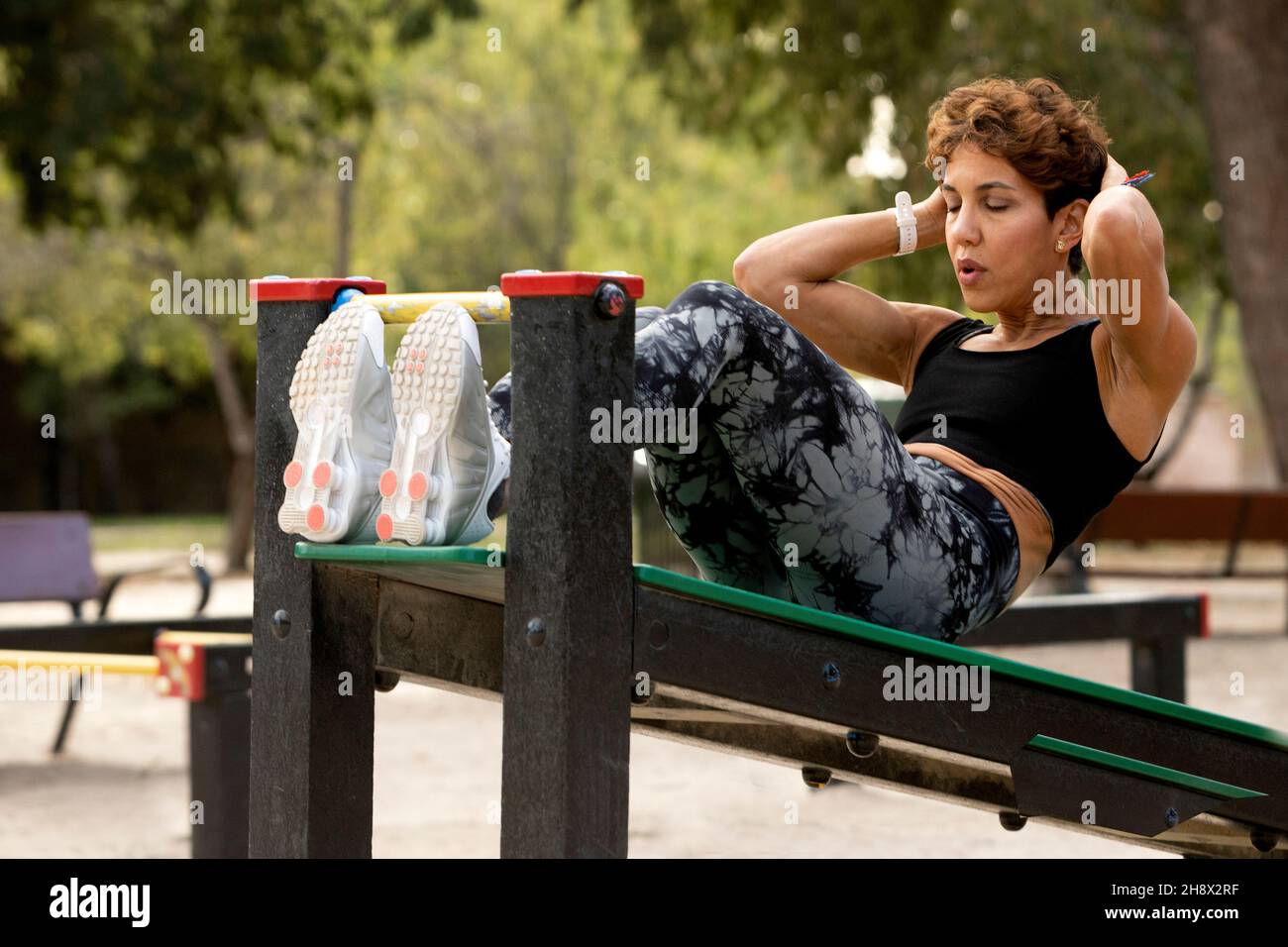 Vista laterale dello sportivo ispanico concentrato con capelli corti in abbigliamento sportivo che fa spingere su panca in campo sportivo nel parco di giorno Foto Stock