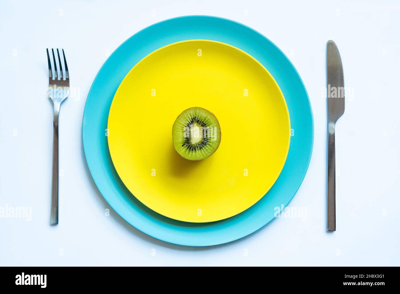 Da sopra di metà di kiwi succosa freschi maturi posti su piatti gialli e blu su superficie bianca Foto Stock