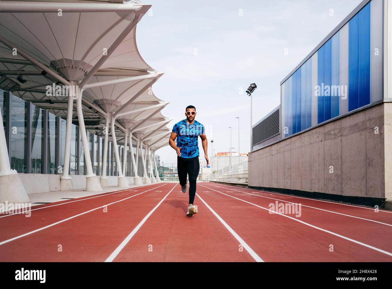 Vista frontale dell'atleta con abbigliamento sportivo e occhiali da sole  che corrono verso la telecamera sulla pista da campo Foto stock - Alamy